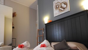 Un lit bien fait, avec des serviettes et des oreillers soigneusement disposés, une échelle en bois et une œuvre d’art encadrée accrochée au mur.