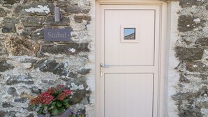 A stone wall with a beige door, a sign reading "Stabal", and a planter with flowers. - Stabal (Ty Croes)