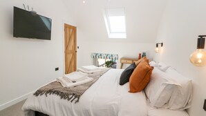 A bedroom with a bed, a TV mounted on the wall, a skylight, and a bedside table with a lamp. - Stabal (Ty Croes)