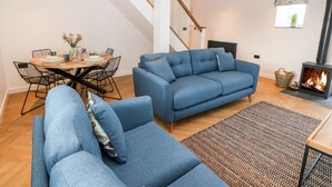 A modern living room with a blue sofa, a dining table set for four, and a fireplace. - Stabal (Ty Croes)