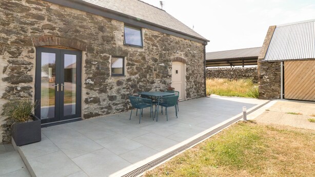 A stone building with a tiled patio, a door, and a small window. - Stabal (Ty Croes)