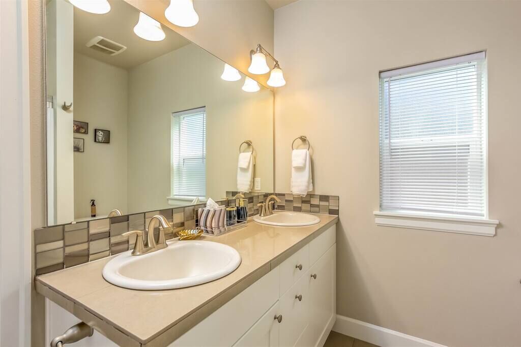 A bathroom with two sinks, a large mirror, and a window with blinds.