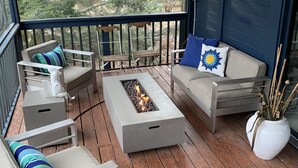 A covered outdoor deck with wooden flooring, grey sofas with blue and white cushions, and a central fire feature. - Cozy House with Hot Tub (Macedon)