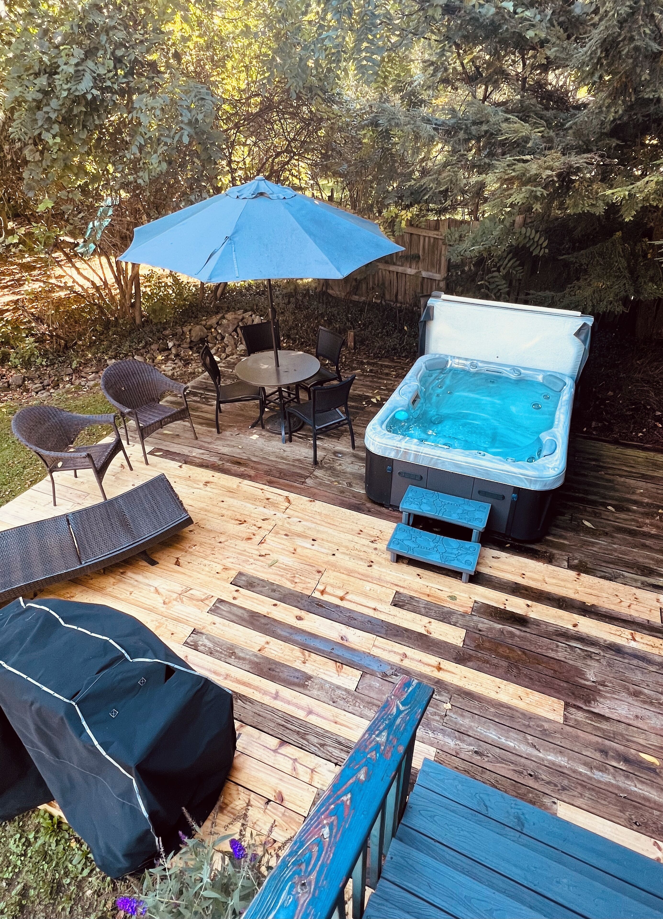 Un patio trasero con un jacuzzi, una mesa de patio techada y sillones de descanso.