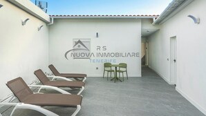 A corridor with a tiled roof, a wall with a logo and text, and a row of sun loungers.