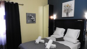A hotel room with a bed, pillows, a headboard, a painting, and a curtain.