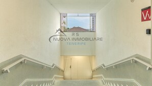 A modern interior with a staircase leading to a door, a logo for 'Nuova Immobiliare Tenerife', and a view of the sea through a window.