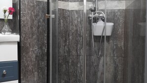 Une salle de bain moderne avec une douche à parois de verre, des murs en marbre et un lavabo blanc.