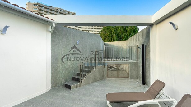 Une terrasse sur le toit au design moderne, comprenant un escalier menant à un niveau supérieur, une porte vitrée et deux fauteuils de relaxation.