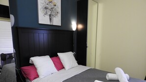 Un lit bien fait, avec des oreillers blancs et roses, une couvre-lit grise et deux serviettes blanches roulées posées sur le lit.