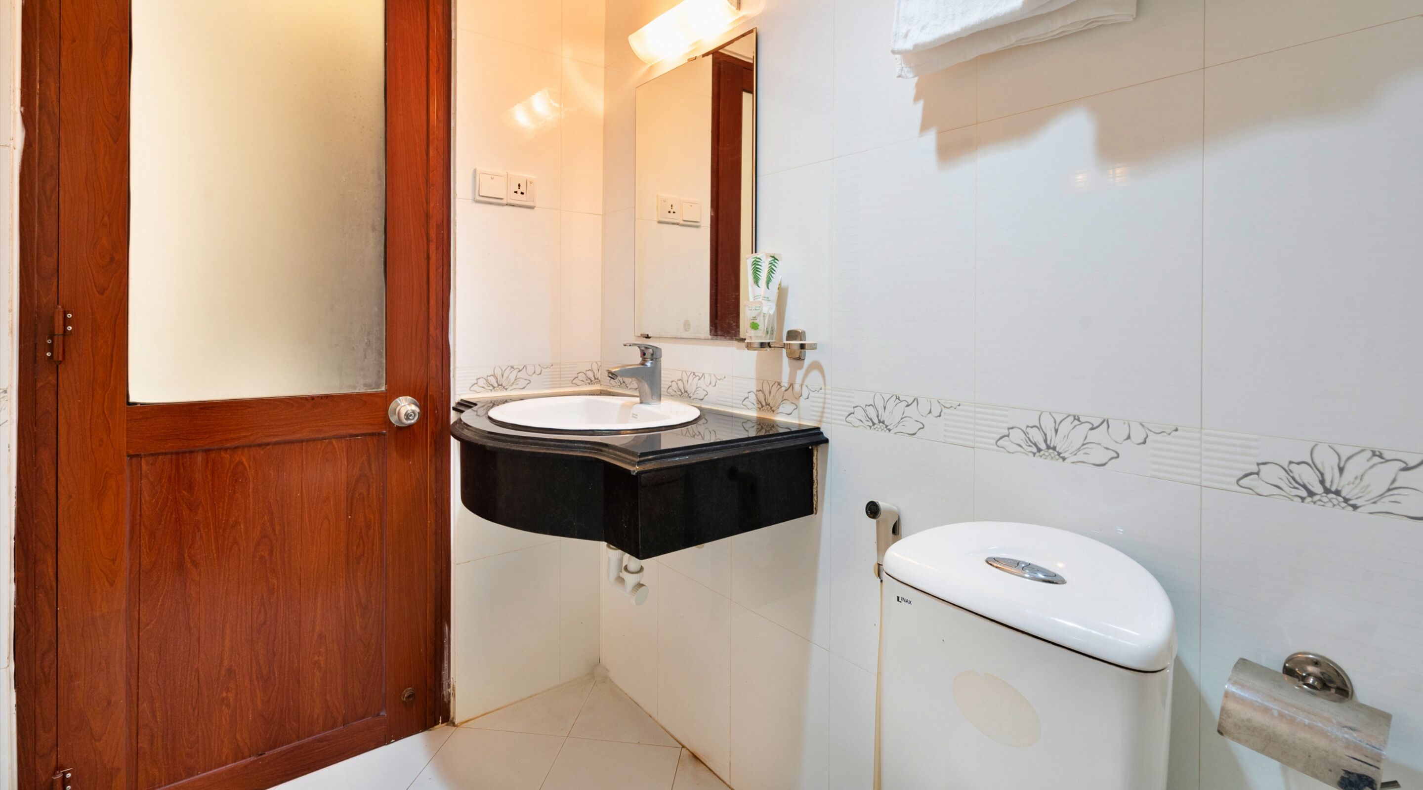 A bathroom with a wooden door, a black sink with a mirror above it, and a white toilet.