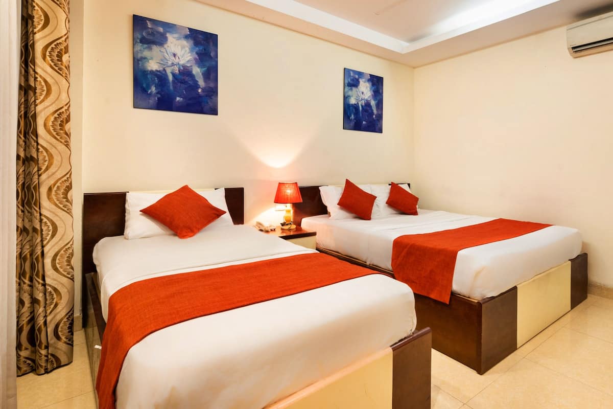Ein Hotelzimmer mit zwei Betten, jeweils mit weißer Bettwäsche und roten Akzenten, einem Nachttisch mit Lampe sowie zwei abstrakten Bildern an der Wand.