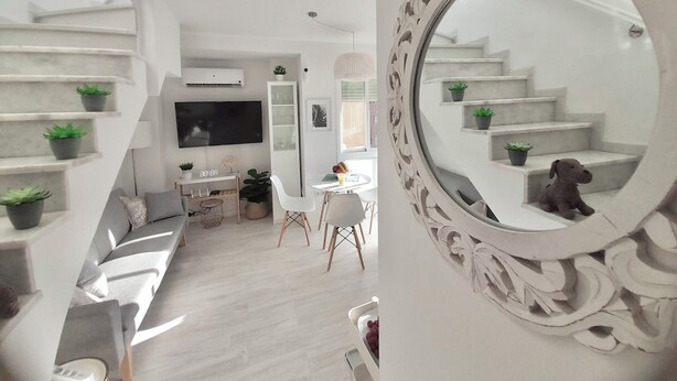 Ein modernes Wohnzimmer mit Treppe, Flachbildfernseher, Essbereich und dekorativem Spiegel.