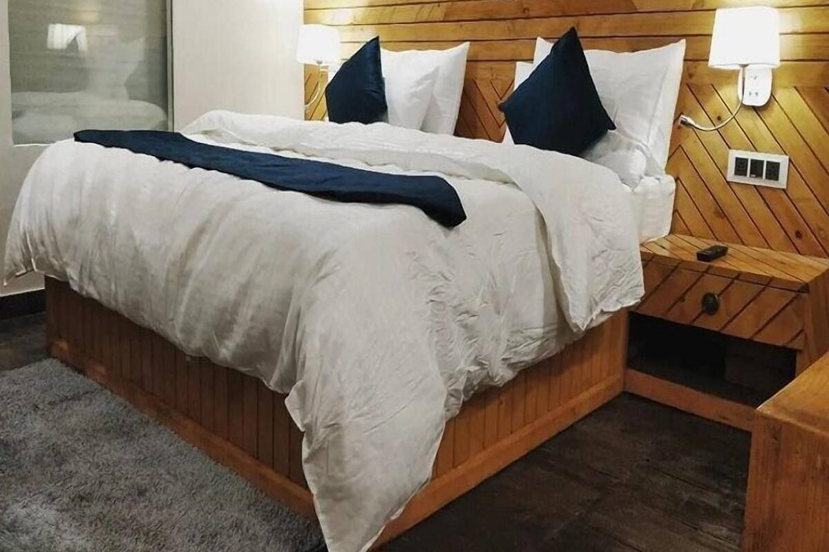 A bed with white bedding, a wooden headboard, and a bedside table with a lamp.