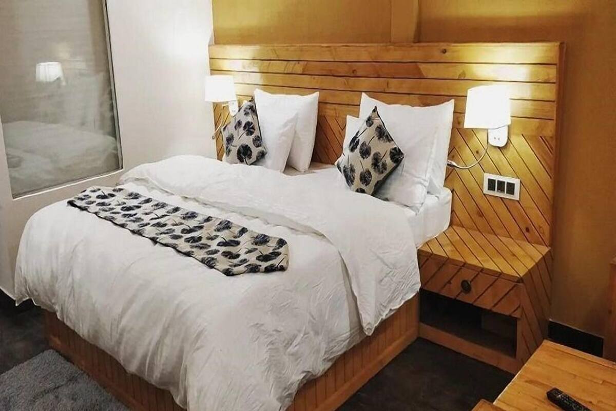 A hotel room with a wooden headboard, white bedding, a patterned throw blanket, and bedside lamps.