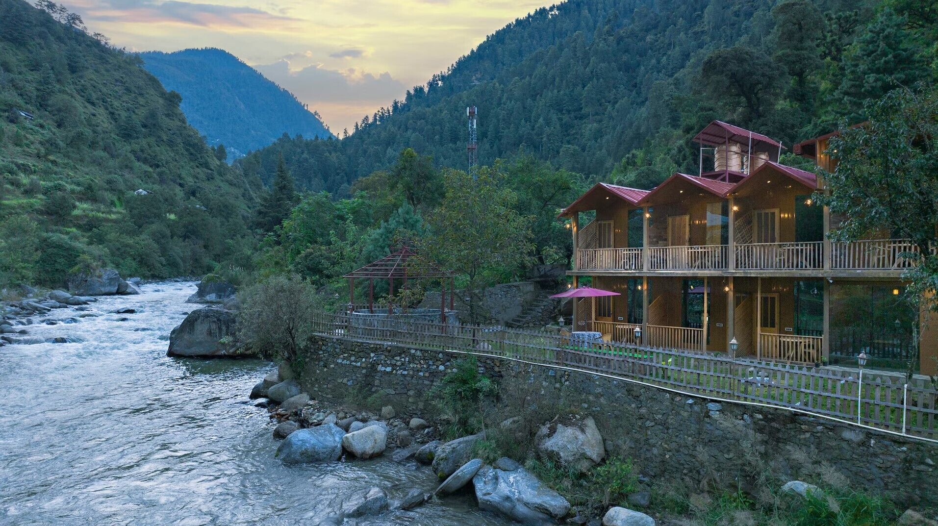 A hotel with a wooden exterior, a balcony, and a view of a river and mountains.