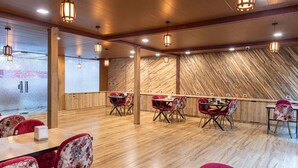 A restaurant with wooden floors, red upholstered chairs, and a long counter with multiple tables. - The Bright Side Resort (Banjar)