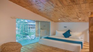 A bedroom with a wooden ceiling, a bed with white and blue bedding, and a view of a building and greenery through a glass door. - The Bright Side Resort (Banjar)
