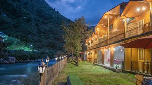 A wooden building with multiple balconies, a river in the background, and a well-lit outdoor area. - The Bright Side Resort (Banjar)