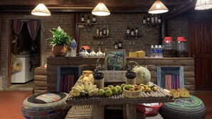 A rustic kitchen with wooden beams, a bar area with shelves of bottles, and a table with fruits and a sign reading "as guest as family". - Sapa Rosie House - Mountain Retreat (Sa Pa)