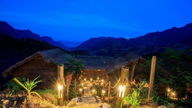 A rustic thatched-roof hut with a stone pathway leading to it, surrounded by greenery and mountains in the background. - Sapa Rosie House - Mountain Retreat (Sa Pa)