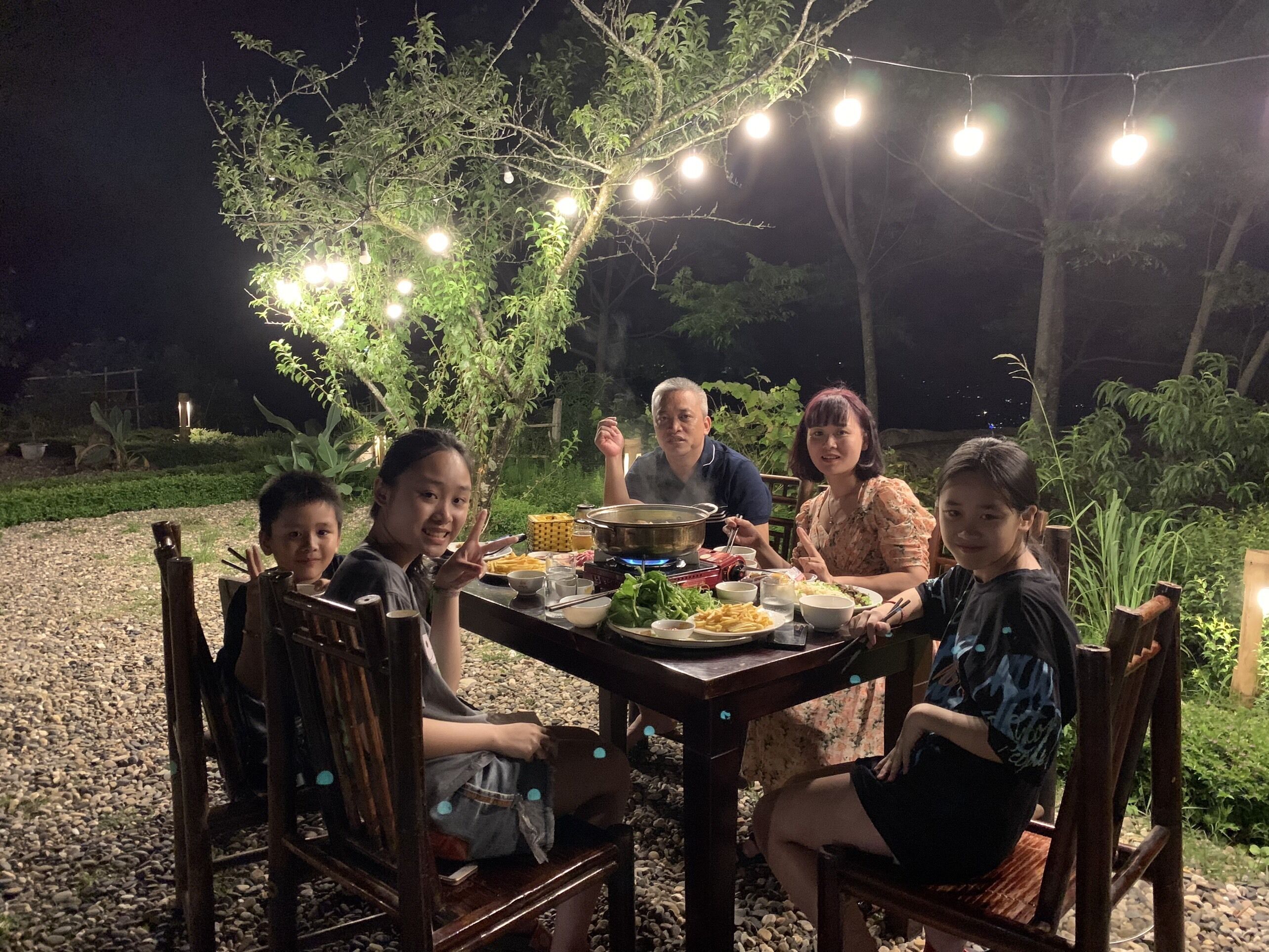 Um grupo de pessoas jantando ao ar livre à noite, com luzes de festa penduradas acima.