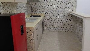 Una cuina compacta amb un frigorífic vermell, una cuina de gas i un salvassecs amb rajoles.