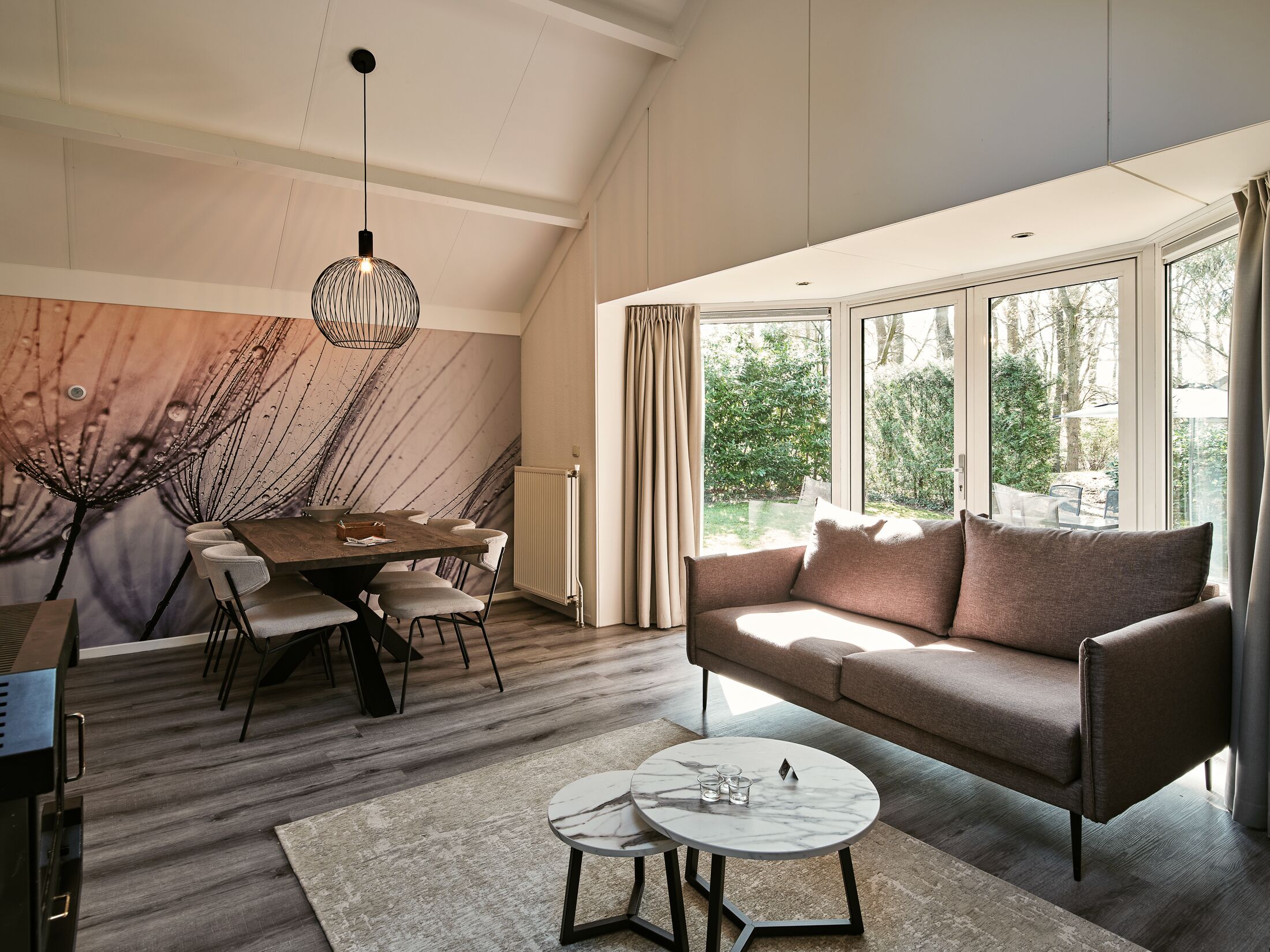 A modern living room with a dining area, large windows, and a view of the outdoors.