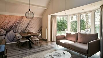 A modern living room with a dining area, large windows, and a view of the outdoors.