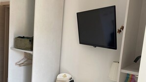 Ein moderner Wohnraum mit Flachbildfernseher an der Wand, einem Glastisch als Schreibtisch, einem gepolsterten Hocker und einem Kleiderhaken.