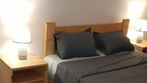 A neatly made bed with a dark-colored bedspread and two pillows, flanked by wooden nightstands with lamps. - 4:ain el Turck Superbe Appartement en Résidence (Aïn El Turk)