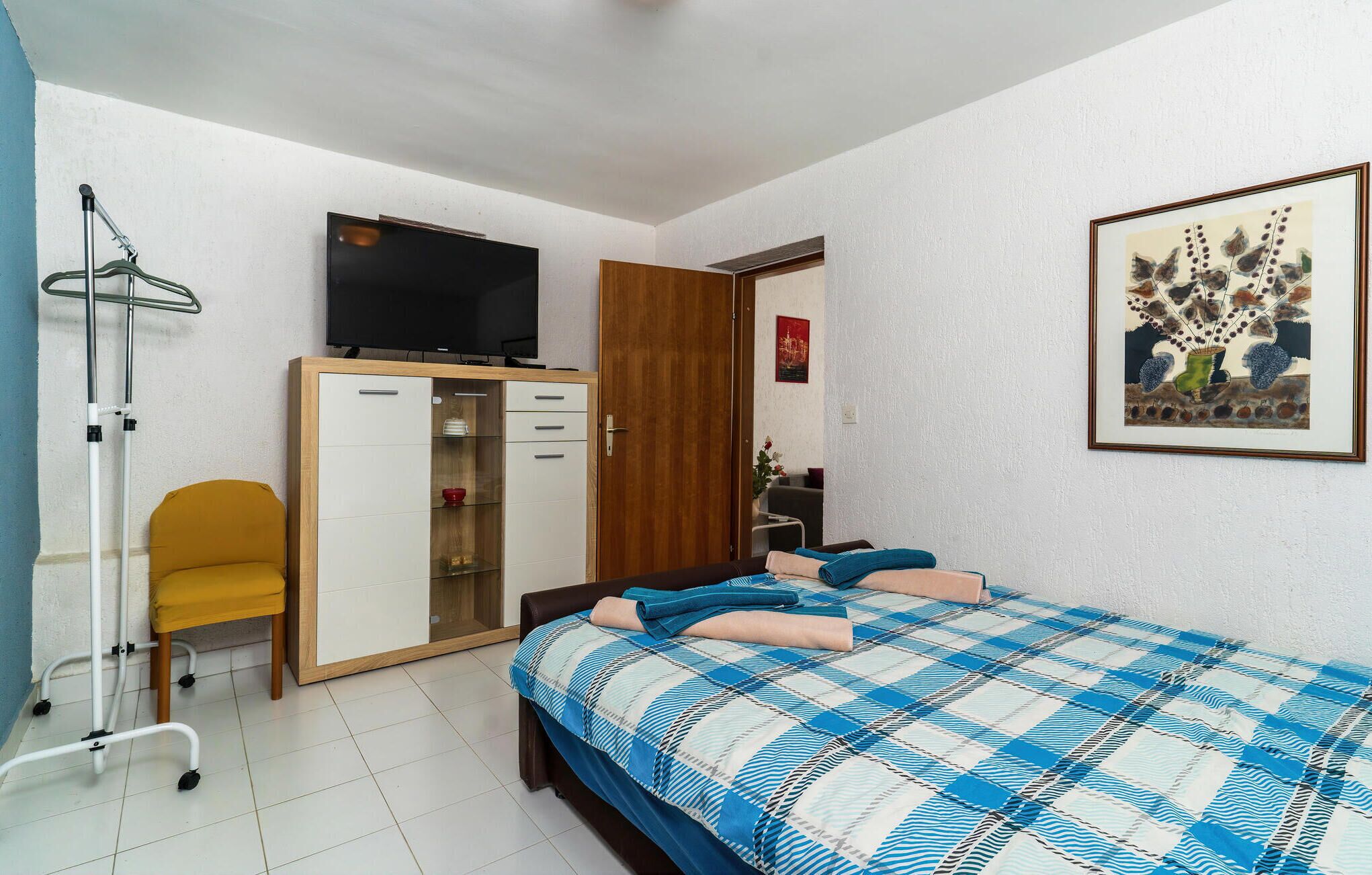 Ein Schlafzimmer mit Bett, Kleiderschrank, Fernseher, Stuhl und einem Bild an der Wand.