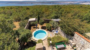 Une piscine entourée de murs de pierre et de verdure, offrant une vue sur la mer et les montagnes lointaines.