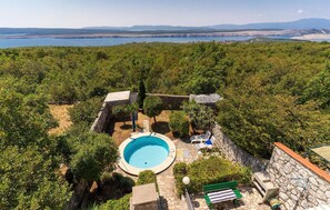 Relax by the serene pool surrounded by lush greenery and a stone wall, set amidst a tranquil forest backdrop.