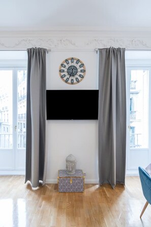 Ein Wohnzimmer mit an der Wand montiertem Fernseher, einer Zieruhr und einer Buddha-Statue auf einer Kommode.