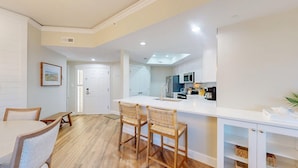 Una cocina moderna con armarios blancos, una isla central con taburetes y un comedor con mesa y sillas de madera.