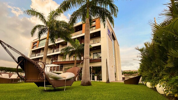 A multi-story hotel with a modern design, featuring a grassy lawn, palm trees, and a hammock. - VM Hotel Cumbuco (Caucaia)