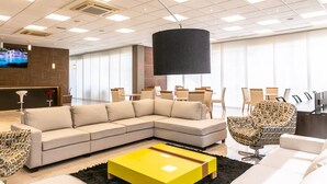 A modern hotel lobby with a sectional sofa, a yellow coffee table, and a patterned armchair. - VM Hotel Cumbuco (Caucaia)