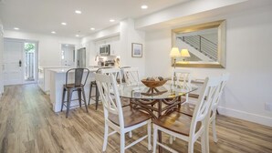 Een moderne keuken met witte kasten, een centraal eiland en een eethoek met een glazen tafel en witte stoelen.