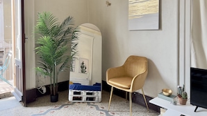 Una stanza con un ampio specchio, una pianta in vaso, un divano blu, una poltrona dorata e un quadro appeso al muro.