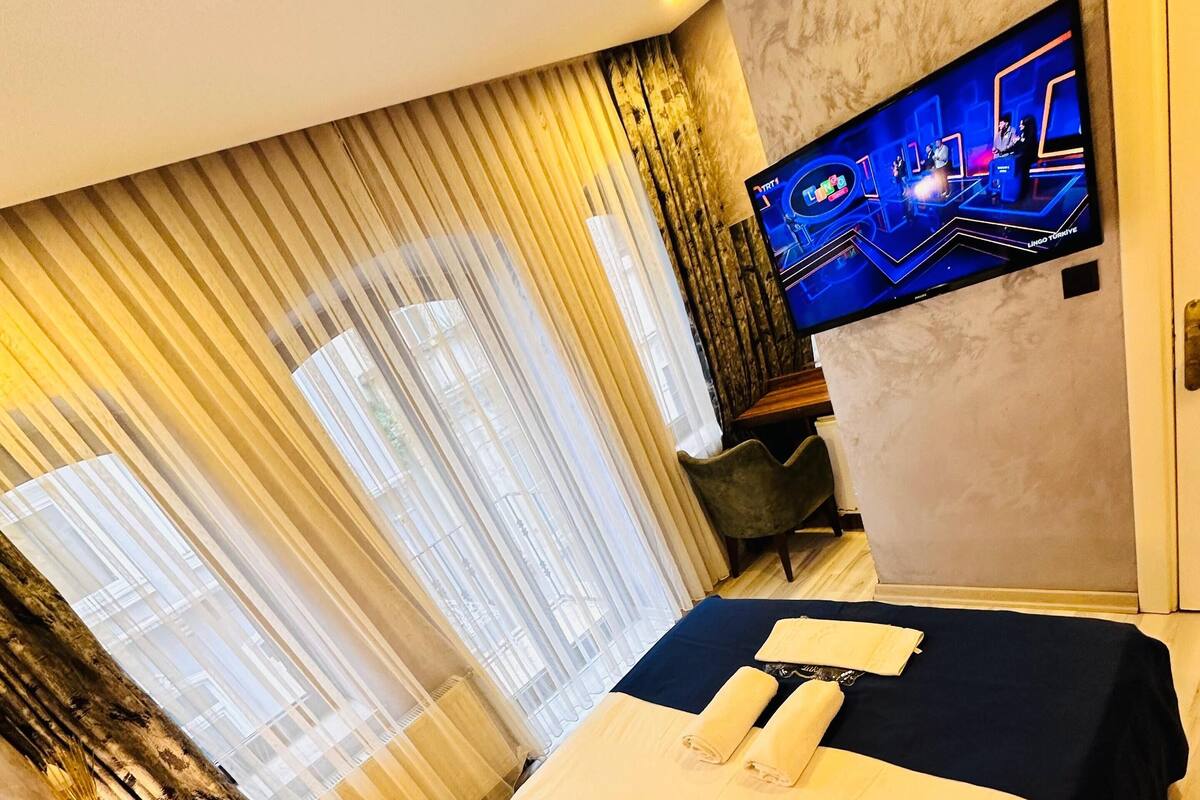 Une chambre d’hôtel avec un grand lit, un téléviseur fixé au mur et une fenêtre avec des rideaux.