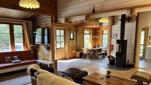 A cozy cabin interior with a wooden dining area, a sofa with a fur throw, and a fireplace.