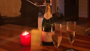 A cozy cabin interior with a wooden interior, a fireplace, a bottle of champagne, and two glasses on a wooden table.