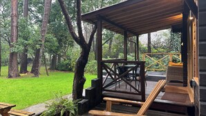 A wooden deck with outdoor seating, surrounded by trees and a grassy area.