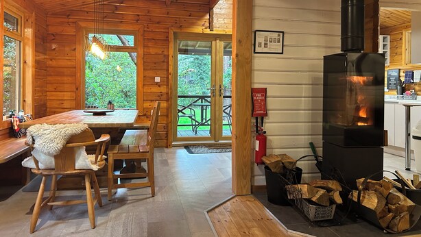A wooden cabin interior with a dining area, a fireplace, and a view of the outdoors.
