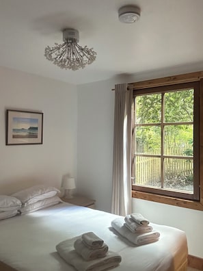 Une chambre à coucher avec un lit, une fenêtre avec des rideaux, une table de chevet avec une lampe et un luminaire au plafond.