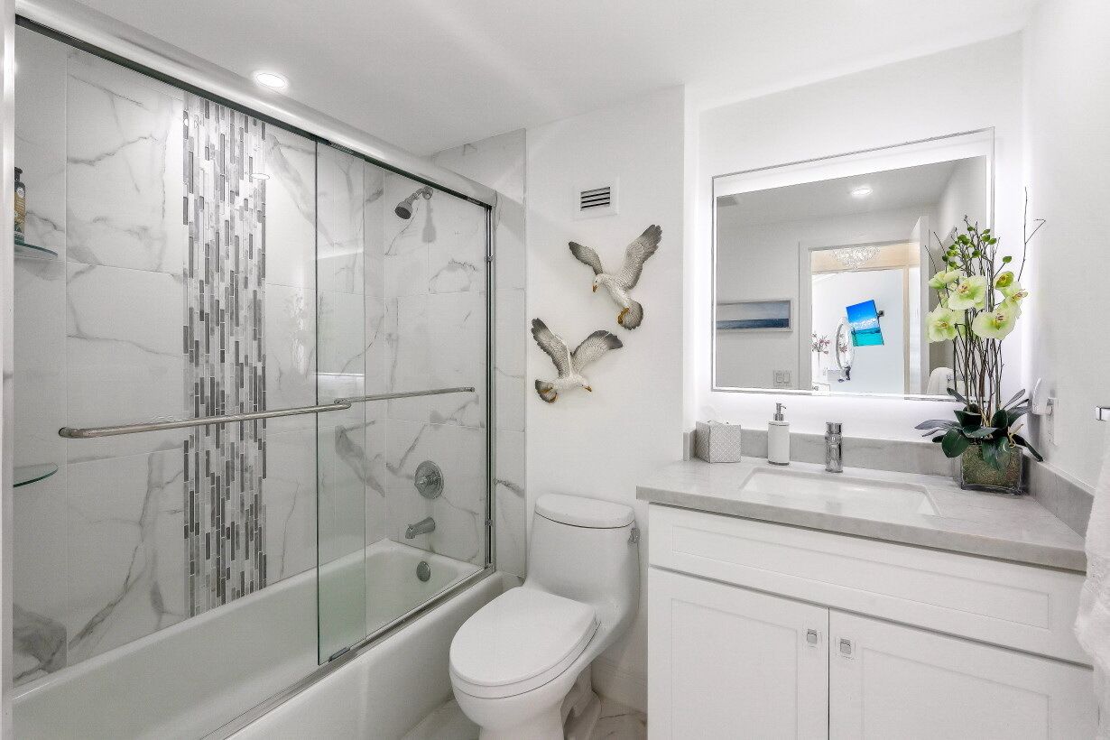Une salle de bain moderne avec une douche à parois de verre, des toilettes blanches et un meuble-lavabo avec un miroir.