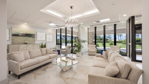 A spacious living room with a beige sofa, a glass coffee table, and a modern chandelier. - Modern Beachfront Condo | Pool, Gym & Tennis (Marco Island)