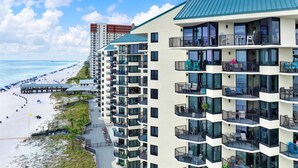 Un hotel frente a la playa con varios balcones, zona de piscina y vistas al mar.