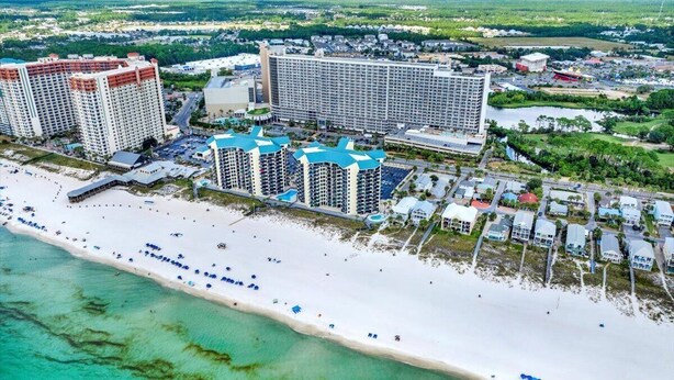 Un complejo turístico costero con varios edificios altos, una playa de arena y un puerto deportivo.